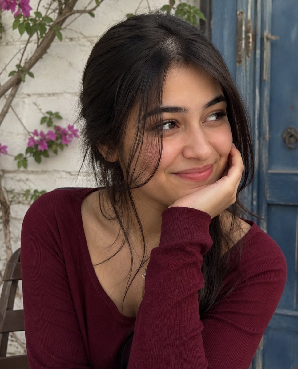 A young woman rests her chin by a bougainvillea-covered wall