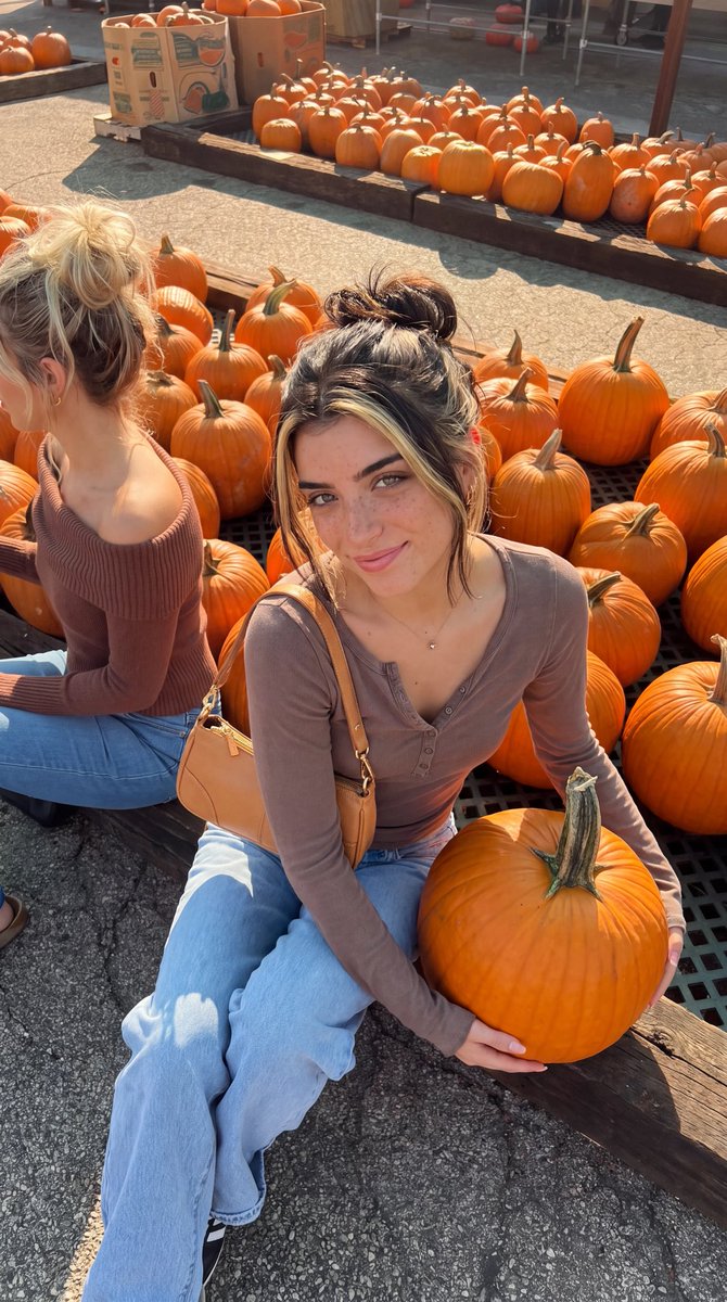 Young Woman Cradles Pumpkin on Wooden Beam at Autumn Market