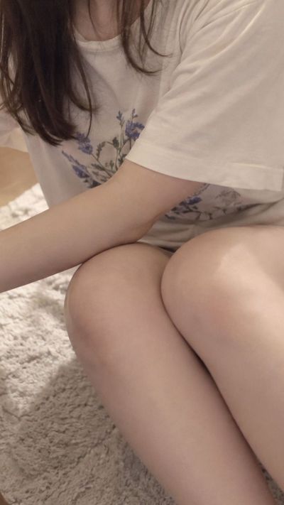 Woman in floral tee sits on rug beside bed reaching for table
