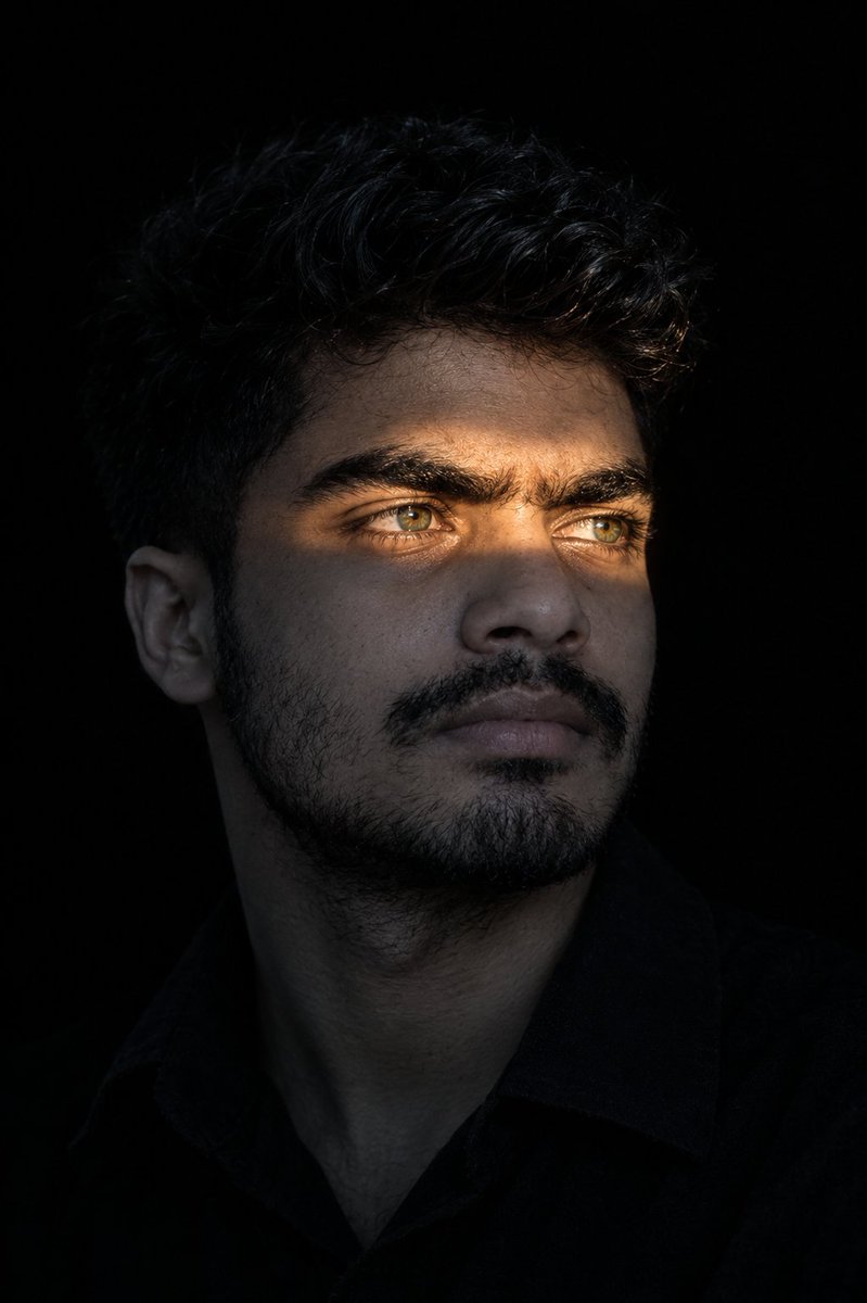 Golden light slices across eyes in dark portrait