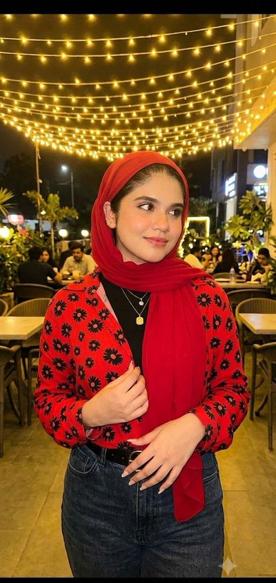 Young woman in red scarf stands under warm fairy lights at night cafe