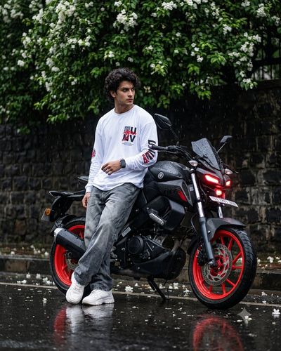 South Indian boy leans on a matte black Yamaha in the rain