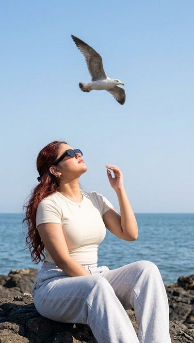 A woman in cream top gazes up at a seagull by the sea