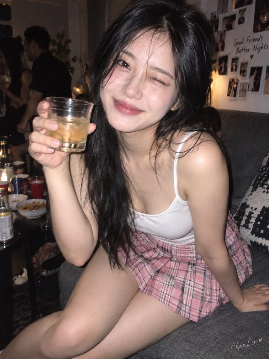 Winking beauty in white tank leans forward on sofa holding shot glass