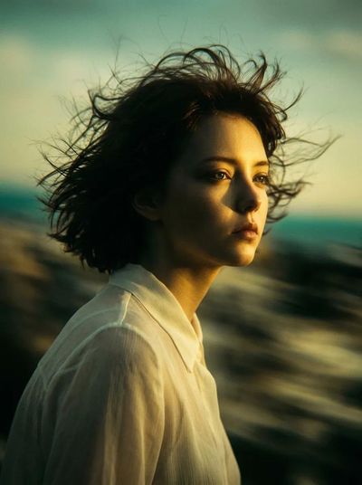 A woman in white blouse stands alone under teal sky