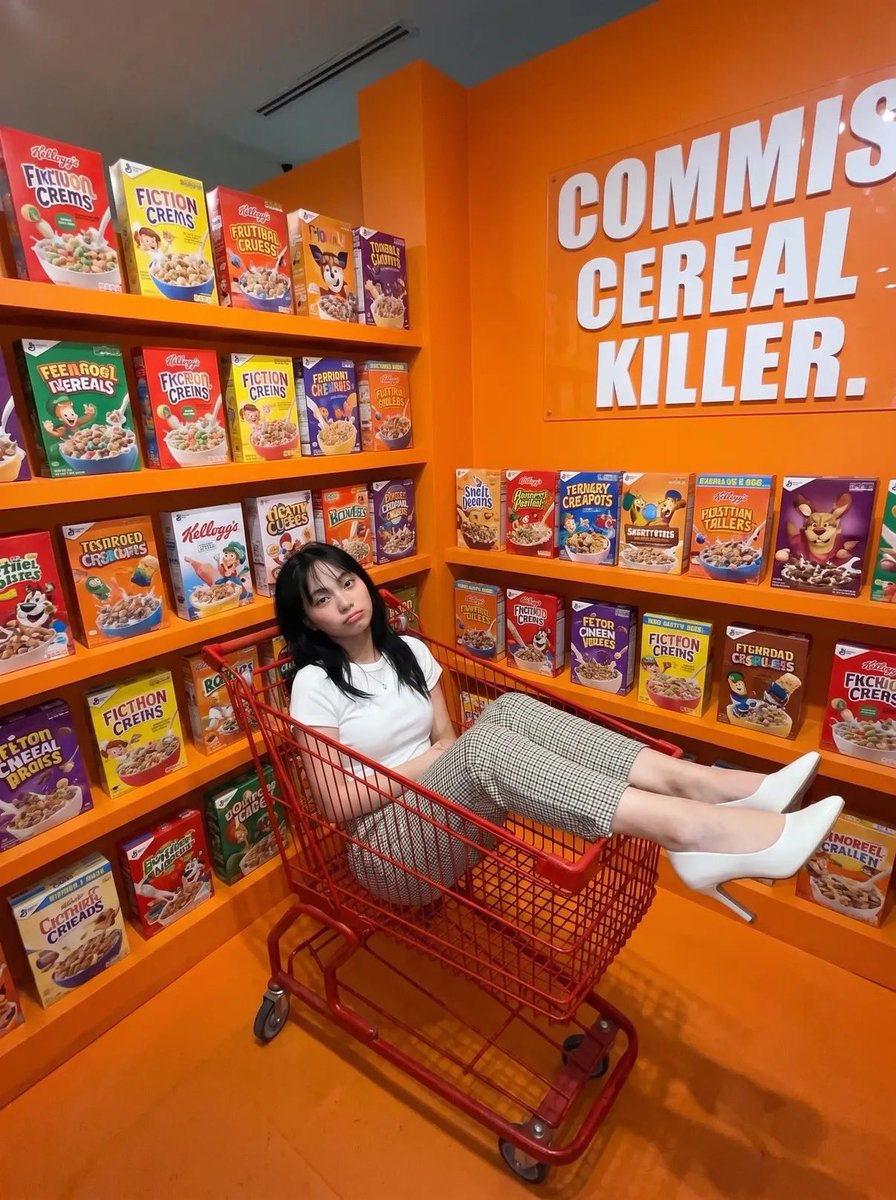 A young woman lounges in a red cart surrounded by orange cereal boxes