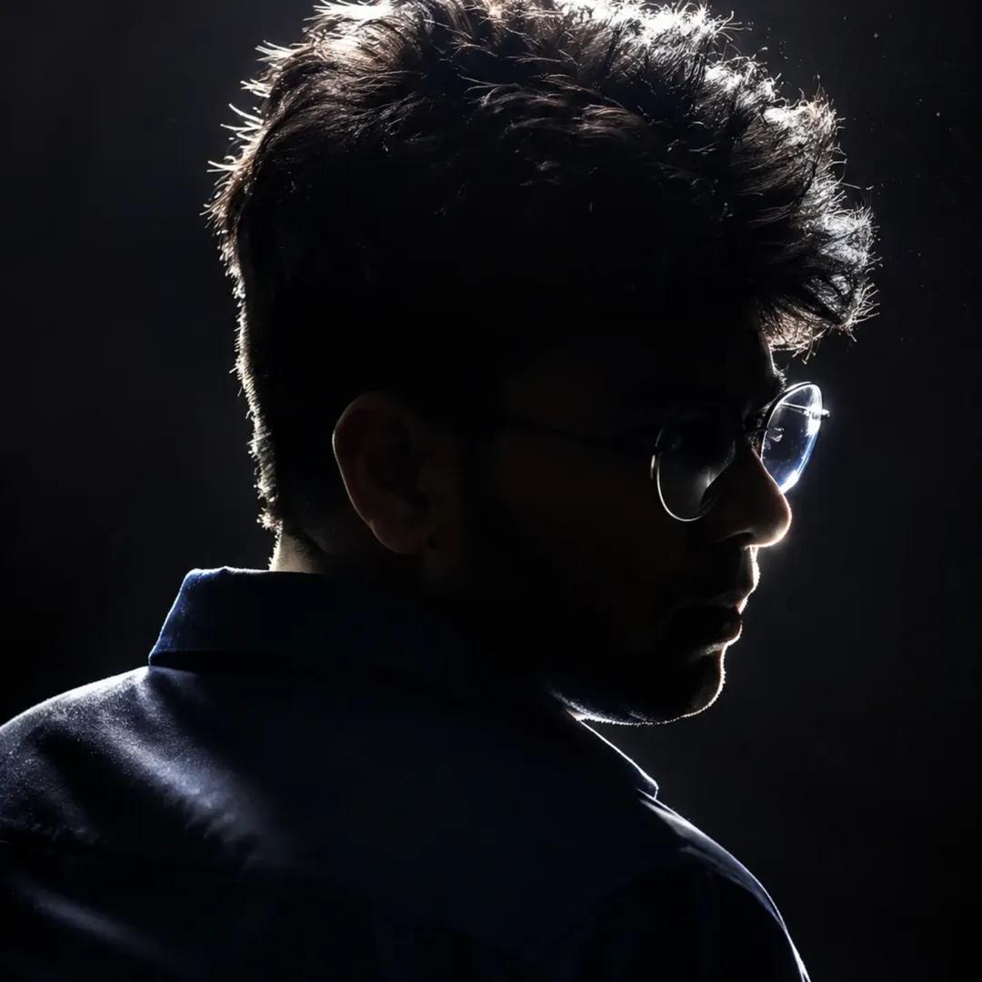 A young man's shadowed profile highlights sharp jawline and rim-lit glasses.