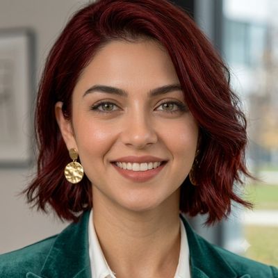 A confident woman in a green blazer smiles warmly indoors.