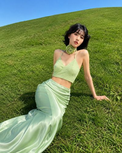 East Asian model reclines on green hill in pastel mint fashion