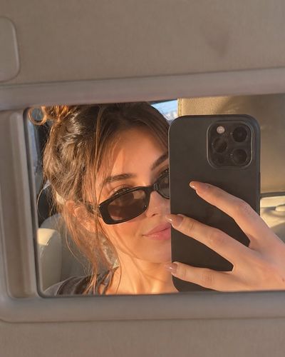 Golden hour selfie through a car mirror with sunglasses and phone