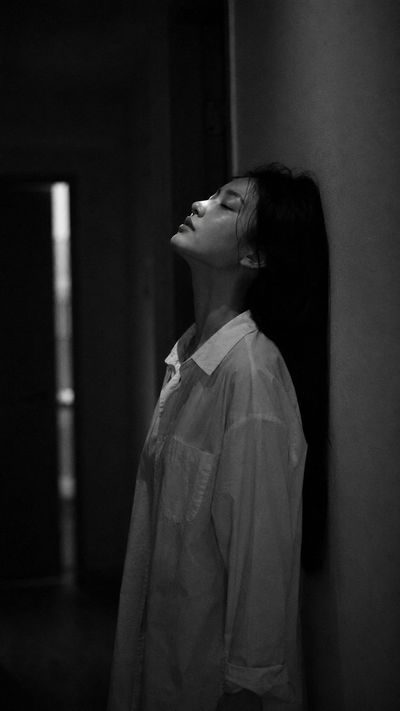 Young woman in near-dark hallway tilts head back with eyes closed