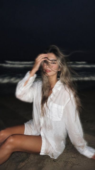Girl sits on dark sand as wind blows her wet hair across her face