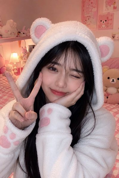 Young woman in a bear hoodie winks in a pastel bedroom
