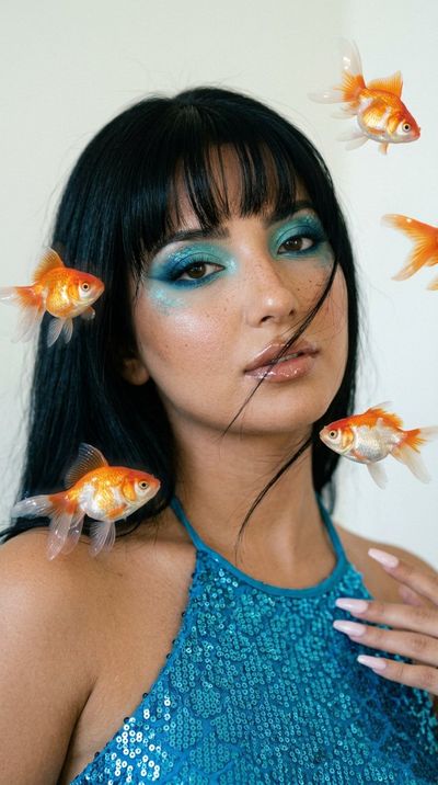 East Asian model with blue aquatic eye makeup poses with floating goldfish