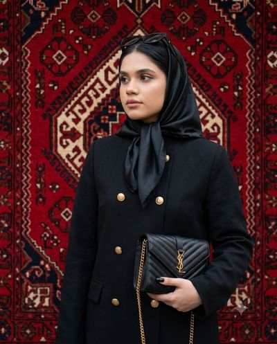 A woman in black stands before a red geometric rug.