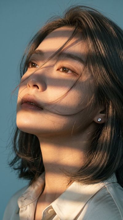 Warm stripes from blinds cast geometric shadows on her face