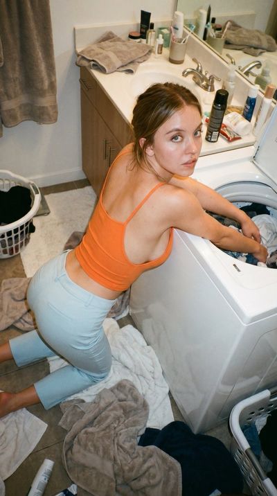 Sydney Sweeney does laundry in a messy bathroom wearing a crop top.