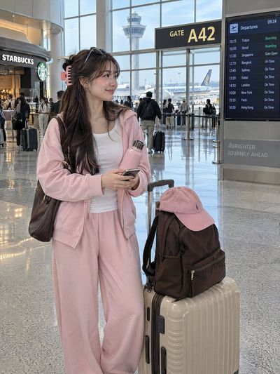 Young woman in pastel pink stands inside bright airport terminal near gate