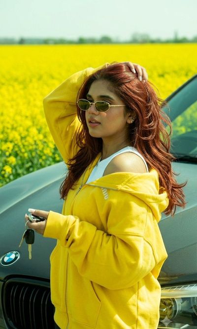 Girl leans against BMW by bright yellow rapeseed field.