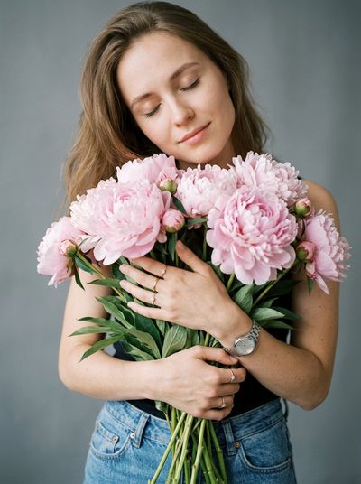 Young woman cradles pale pink peonies in a serene studio portrait