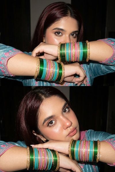 A woman in bangles poses with arms raised and eyes exposed