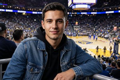 Young man in denim jacket watches basketball game from stands