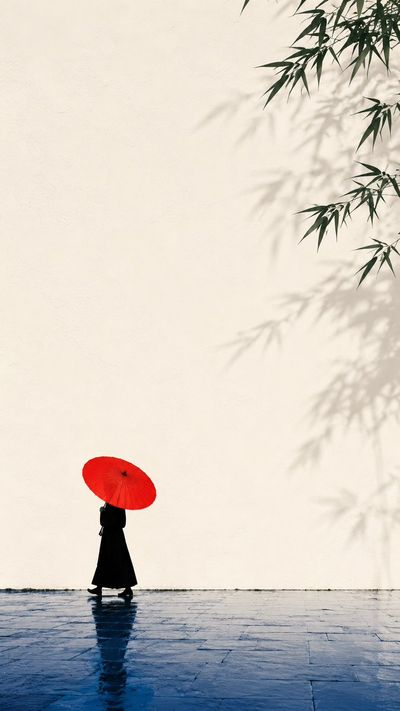 A red oil-paper umbrella glows against a warm white wall after rain