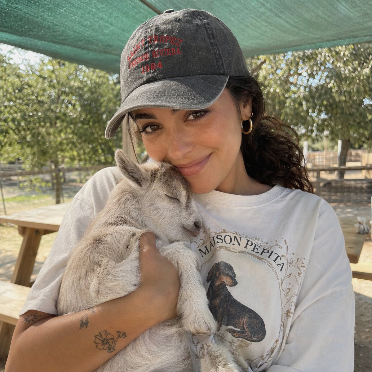 A woman in a cap holds a sleeping baby goat on a sunny farm