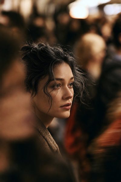 A lone woman in a wool coat walks through a crowded city street at night.