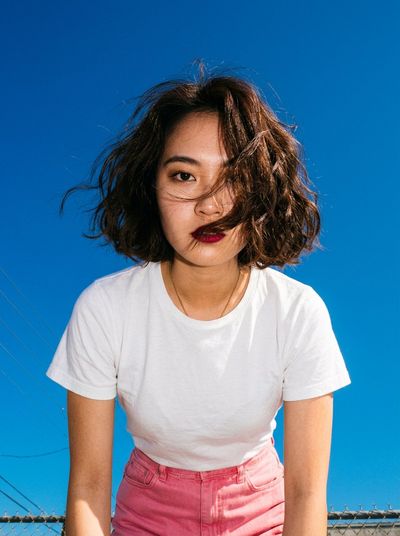 Young woman in pink skirt towers against deep electric blue sky