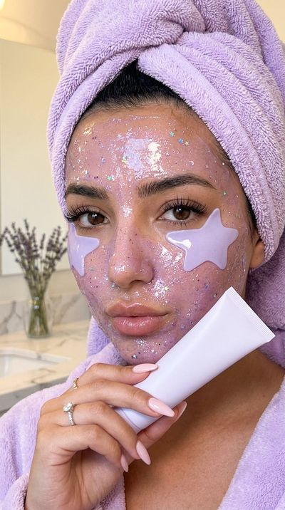 Woman with lavender glitter mask holds white tube near lips