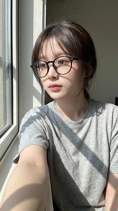 Young woman in glasses gazes contemplatively by sunlit window