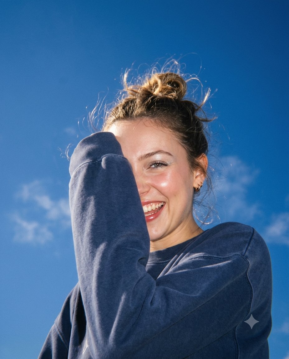 She laughs shielding her face under a deep blue sky