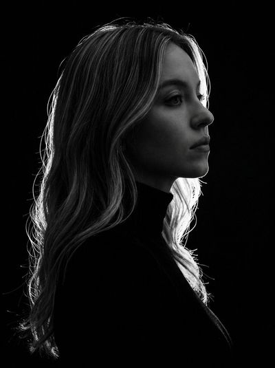 Side-lit woman in profile wears black turtleneck against dark backdrop