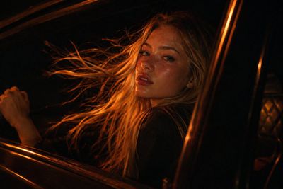 Blonde Woman Leans Out Car Window in Amber Night Glow