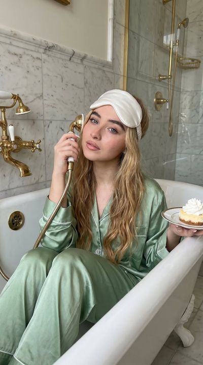 Young woman in satin pajamas holds dessert while showering in vintage bathtub