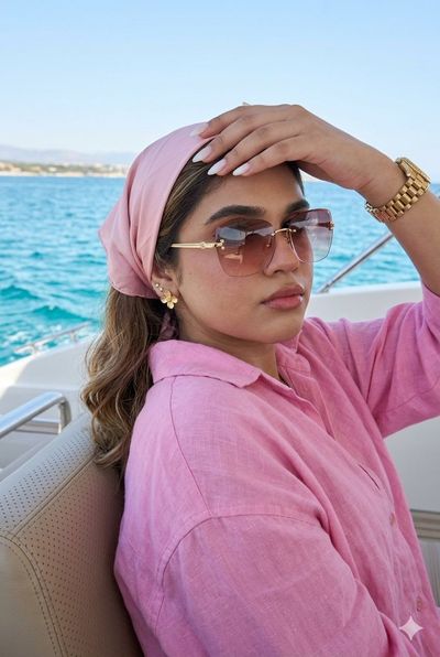 A woman in a pink linen shirt adjusts her sunglasses on a yacht