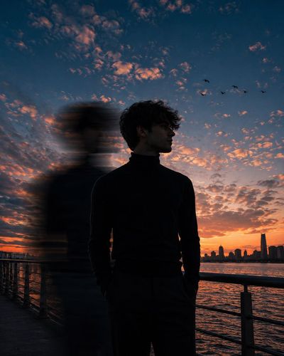 A young man in a turtleneck gazes at the sunset horizon