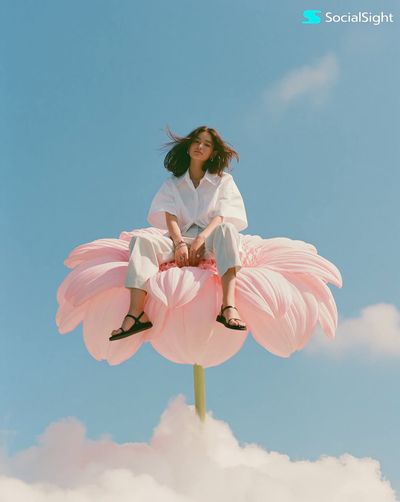 Model sits serenely on a giant pink flower above clouds