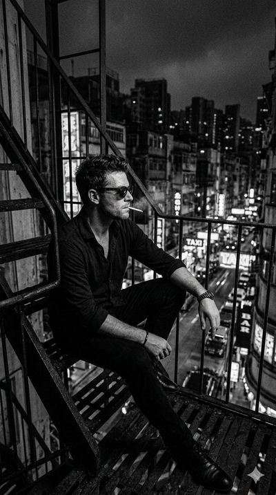 Noir Reflection: Man on Fire Escape Overlooking Neon Cityscape