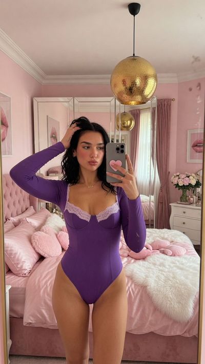 Woman in black lace bodysuit takes mirror selfie in pink bedroom