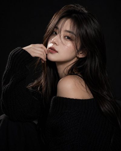 A stylish woman in a black sweater poses with mysterious grace.