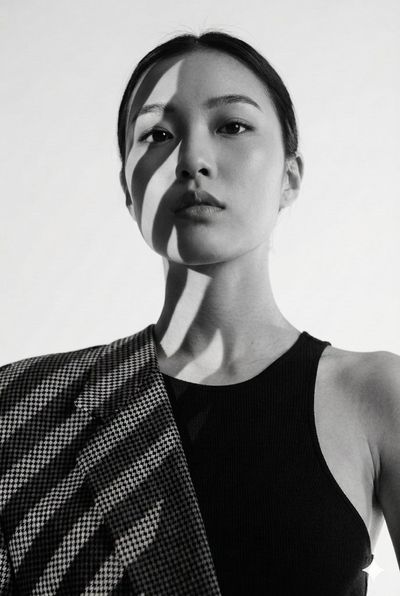 A woman in a houndstooth blazer poses with dramatic shadows