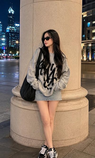A stylish woman in a grey sweater poses by a pillar at night