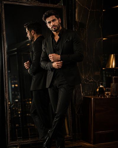 Sharp-suited man adjusts cufflink before a mirror in dark penthouse