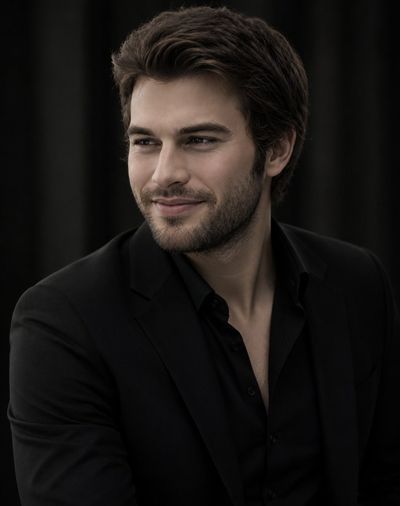 Confident man in tailored black suit smiles gently in studio portrait