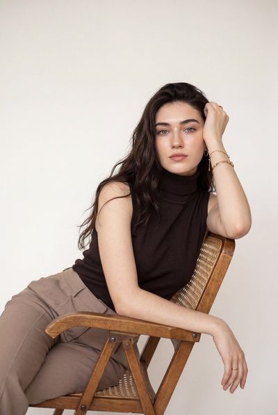Woman leans on wooden chair in minimalist luxury portrait