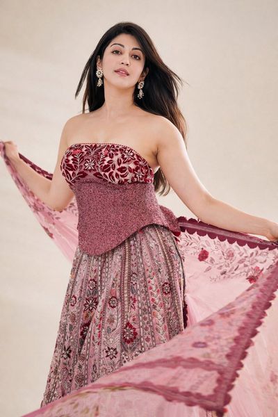 A woman in maroon stands gracefully holding flowing pink fabric.
