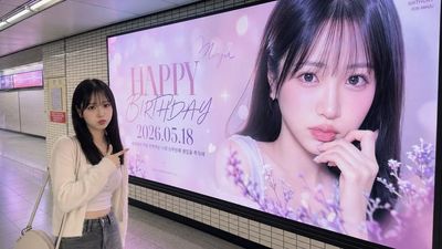 A fan stands in Seoul subway pointing at his own billboard ad