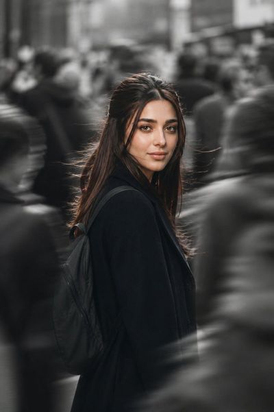 Woman in black coat pauses amid blurred city crowd